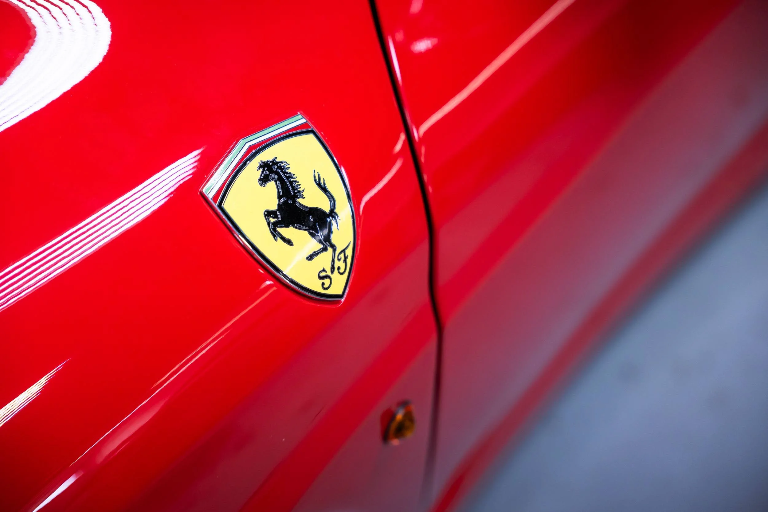 Close-up of a red Ferrari car showing the Ferrari emblem with a black prancing horse on a yellow shield, surrounded by a silver border.