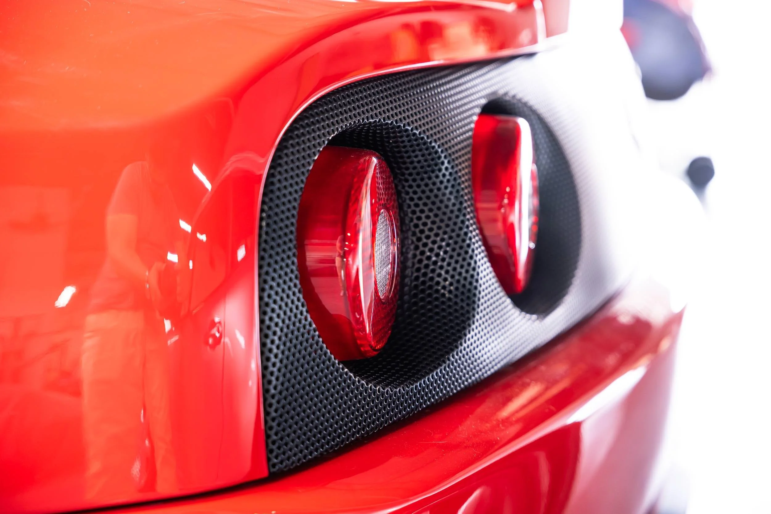 Close-up of a red sports car's rear vent with black mesh and circular tail lights.