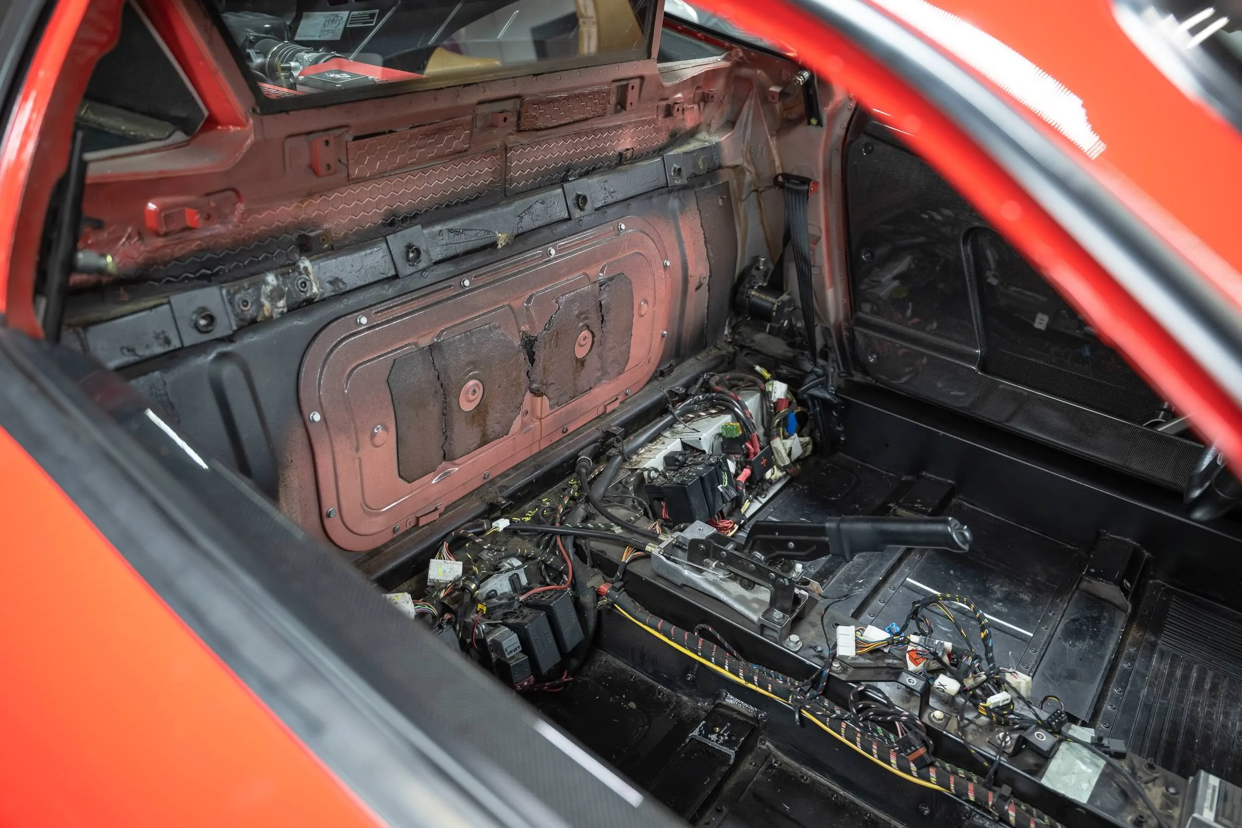 The interior of a race car with the dashboard and wiring exposed, showing an unfinished interior with missing panels and electrical components.