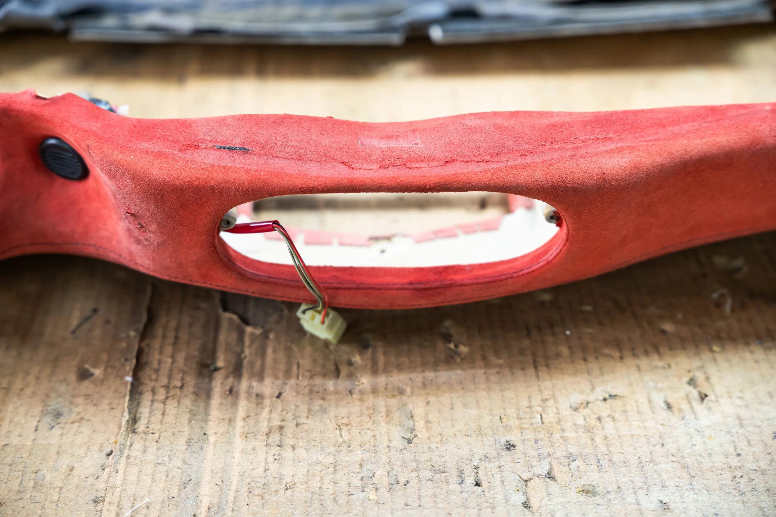 A close-up view of a redish-pink plastic object with a cutout handle, black buttons, and some electrical wiring, resting on a wooden surface.