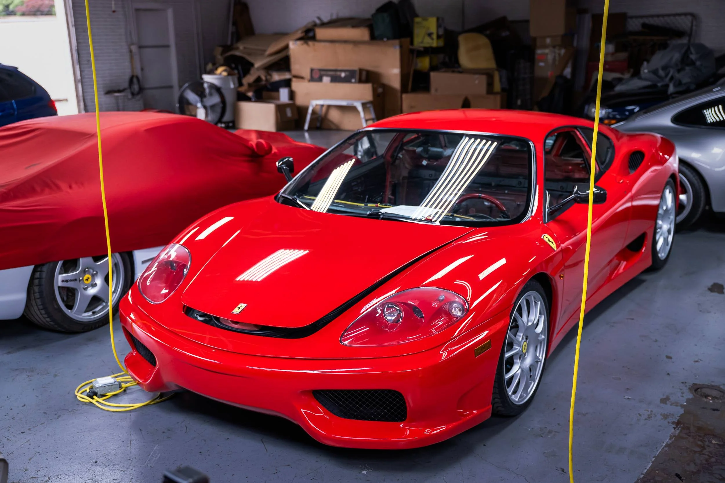 Red Ferrari sports car parked inside a garage alongside other cars, with yellow charging cables linked to it.