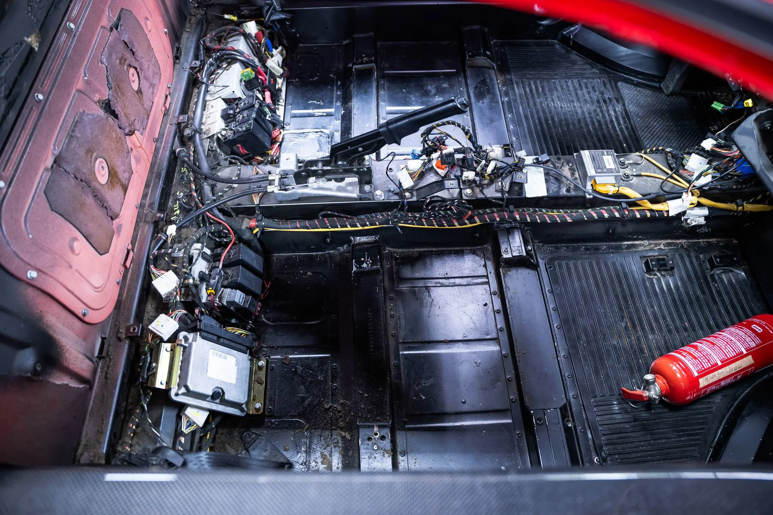 Interior of a car with seats removed, revealing wiring, electronic components, and a fire extinguisher on the passenger side.