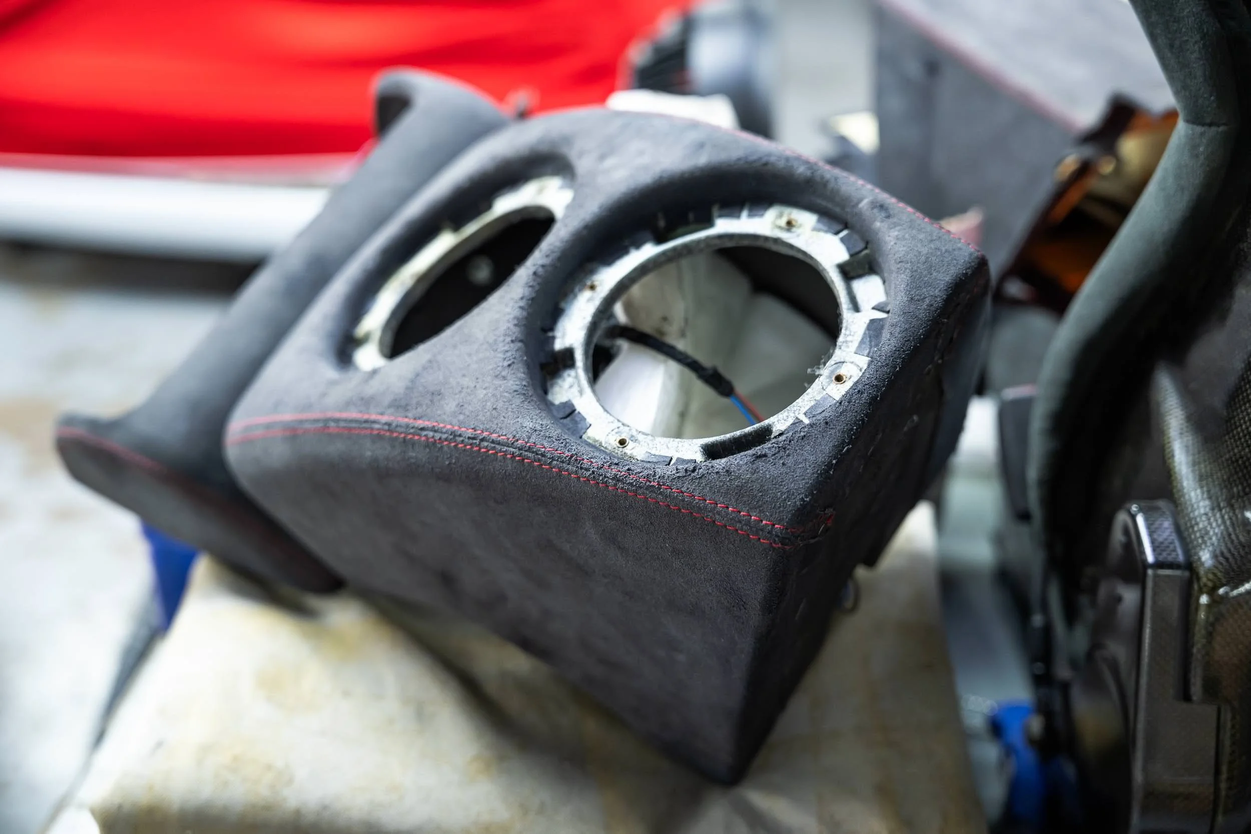 Close-up of a black, textured motorcycle fuel tank with red stitching, showing internal wiring and mounting hardware.