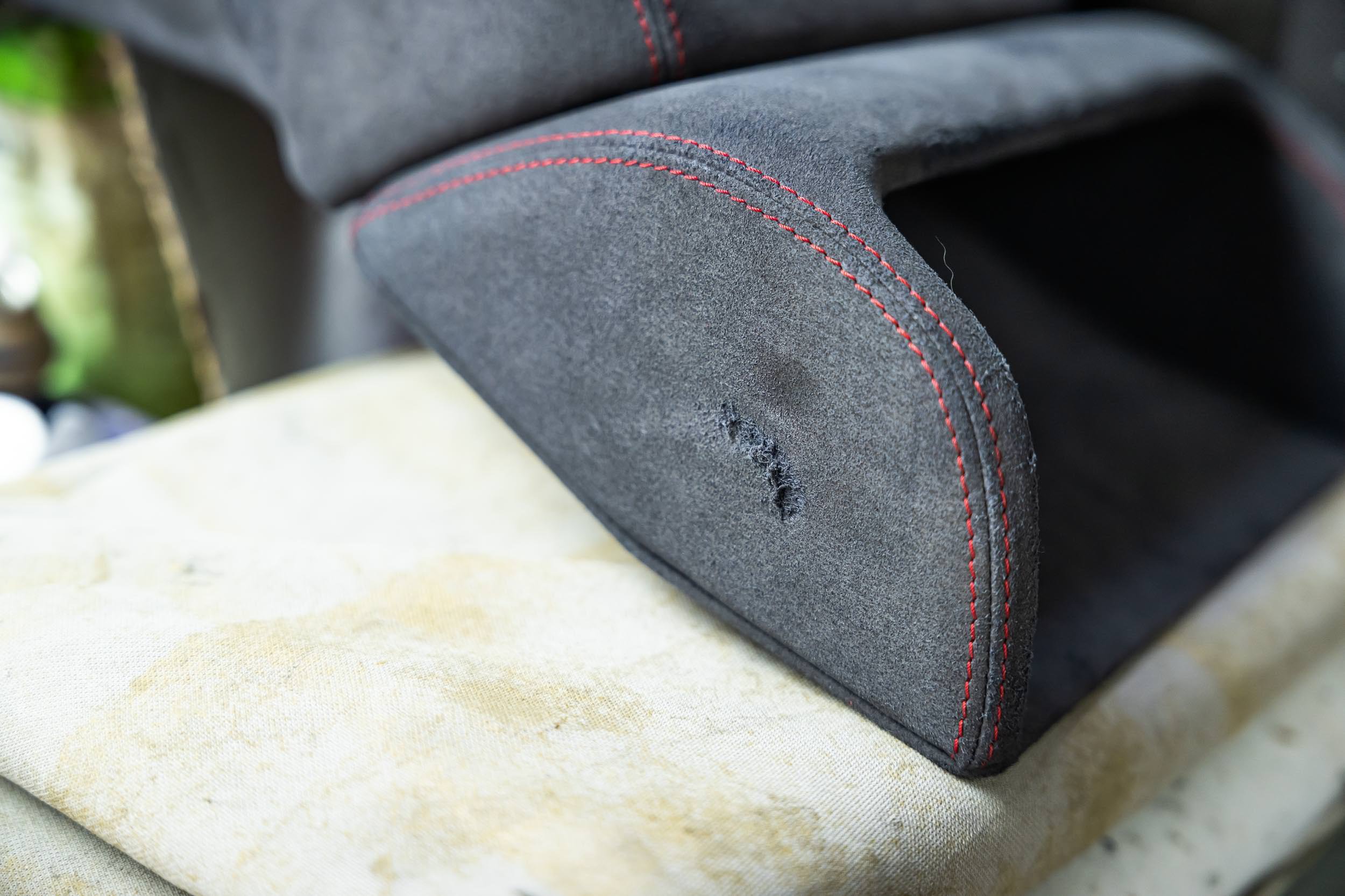 Close-up of the backrest of a black car seat with red stitching, showing some wear and tear on the fabric.
