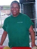 Man in a green T-shirt standing outdoors near a black wire fence.