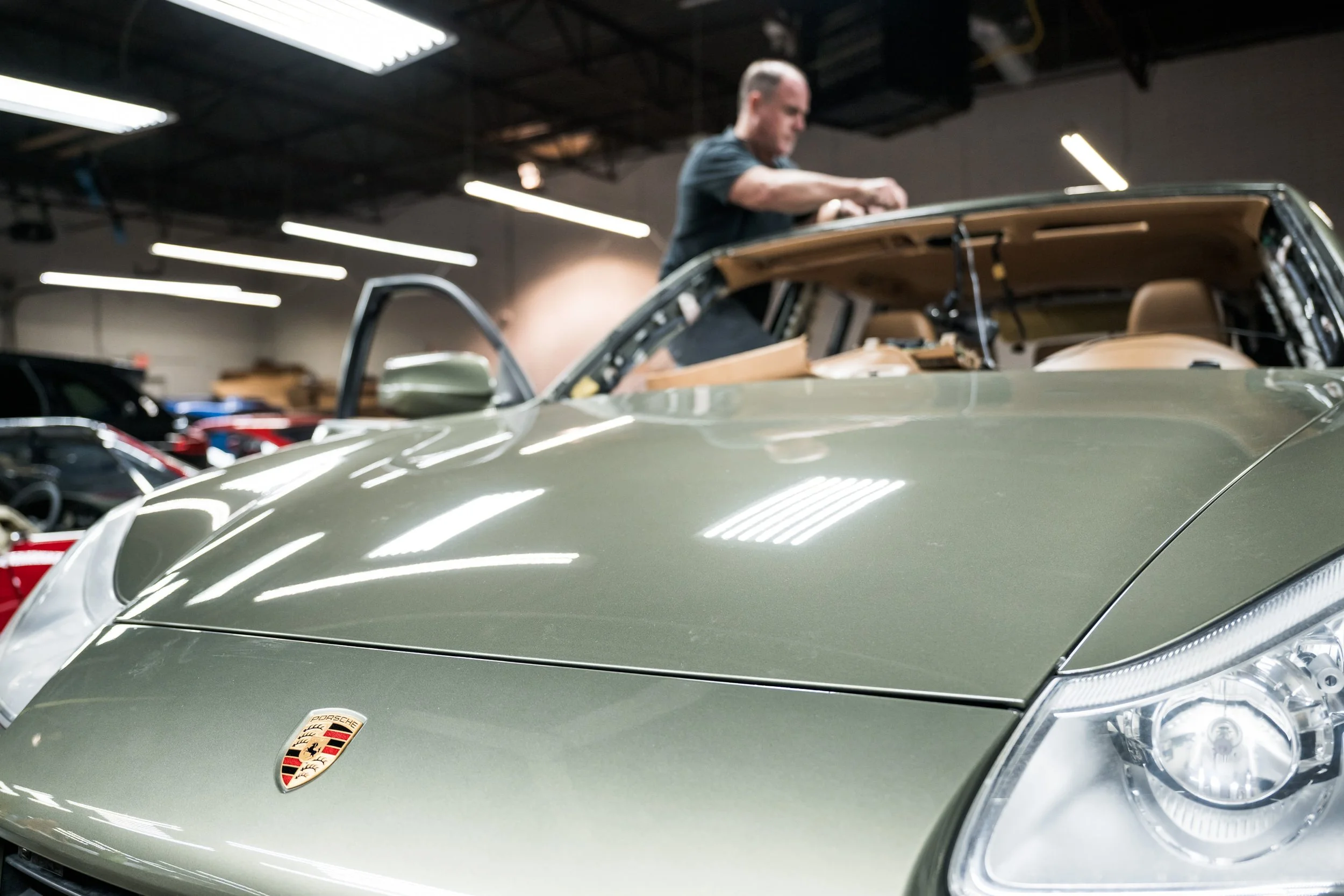 A man working on the engine of a silver Porsche car inside a garage or workshop.