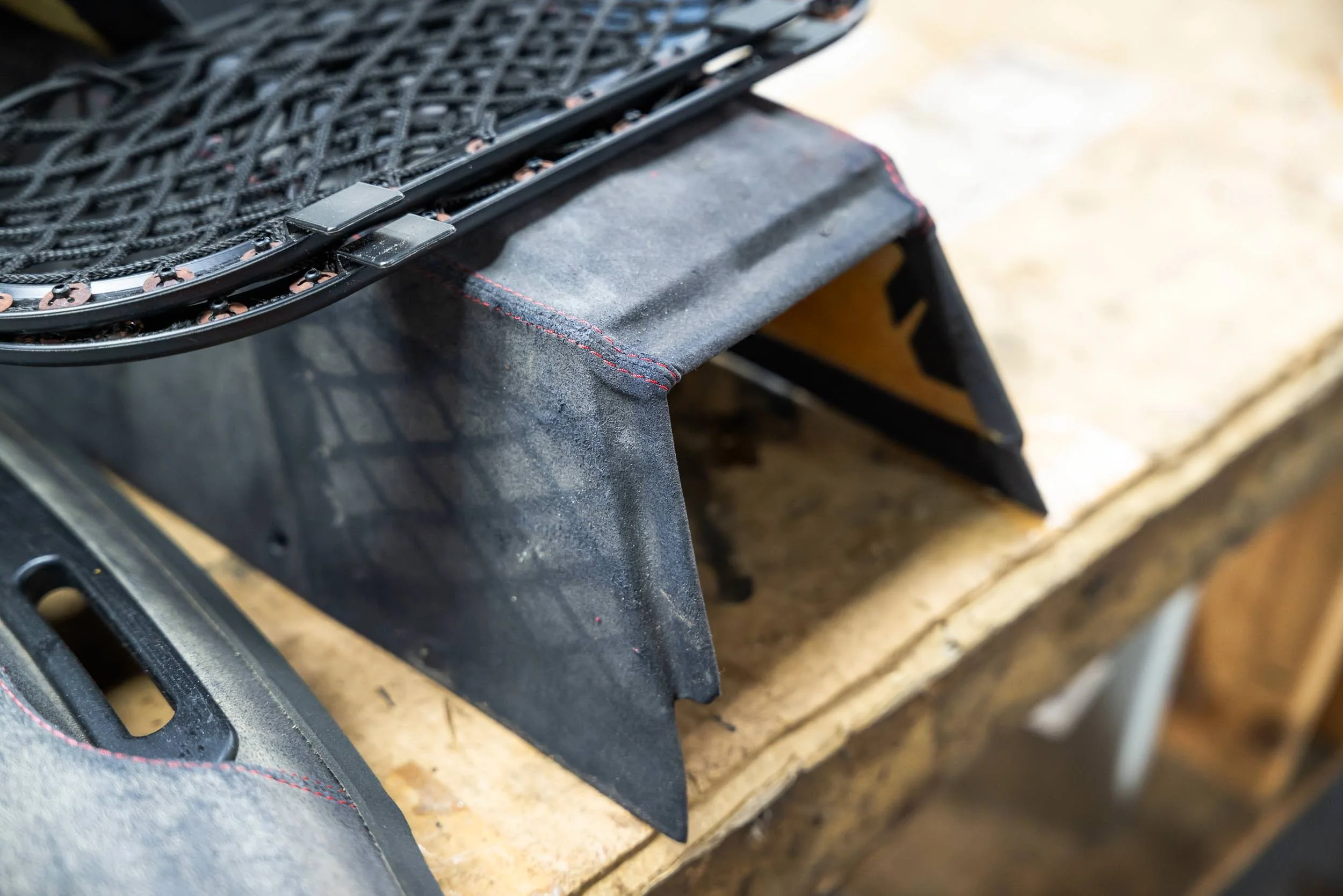 Close-up of a black tennis racket resting on a black padded surface with red stitching, positioned on a wooden surface.
