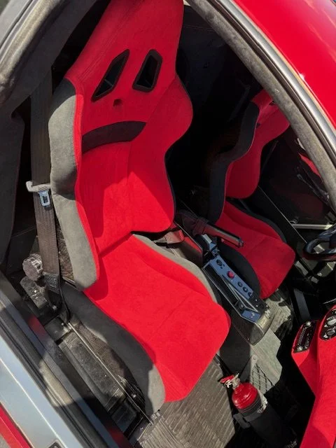 Red racing seats inside a car interior with a fire extinguisher attached to the floor.