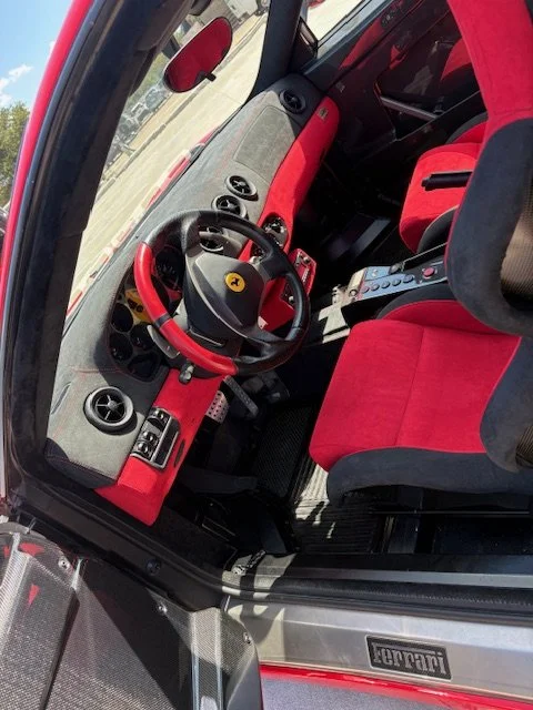 Interior of a race car with red and black racing seats, a racing steering wheel, and a digital display on the center console.