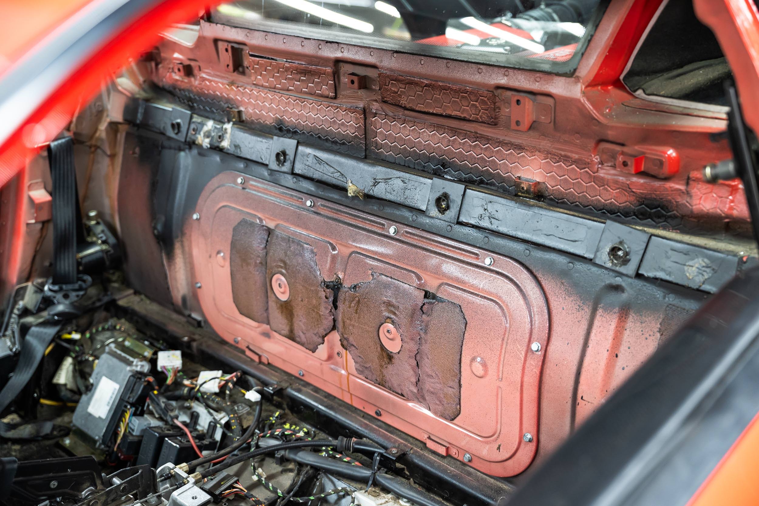 The interior of a vehicle with the dashboard and panels removed, exposing wiring and metal components.
