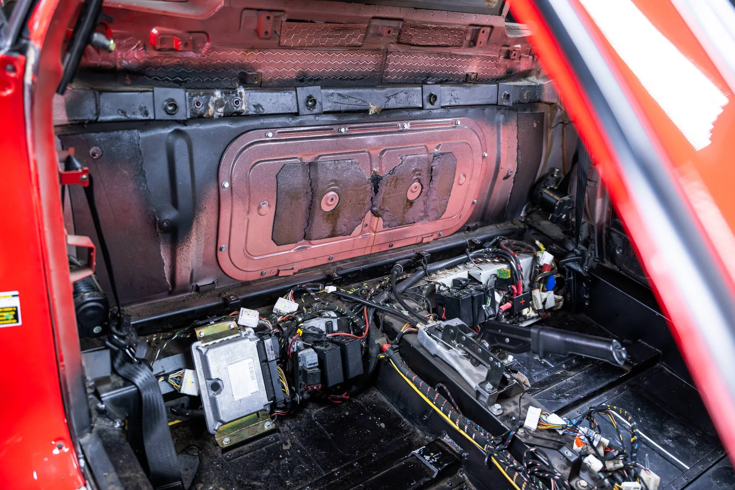 The image shows the interior of a car with the dashboard removed, exposing the wiring, electronic components, and metal framework inside the vehicle.