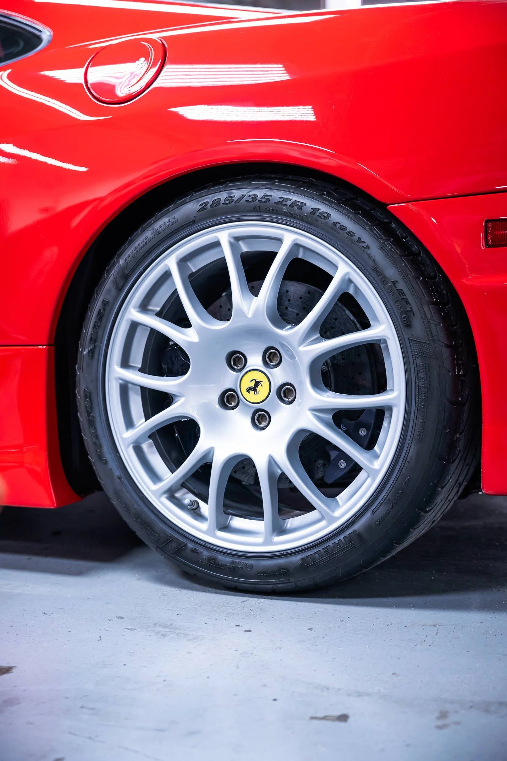 Close-up of a red sports car's rear wheel with silver alloy rim and Michelin tire, displaying the Ferrari logo on the wheel hub.