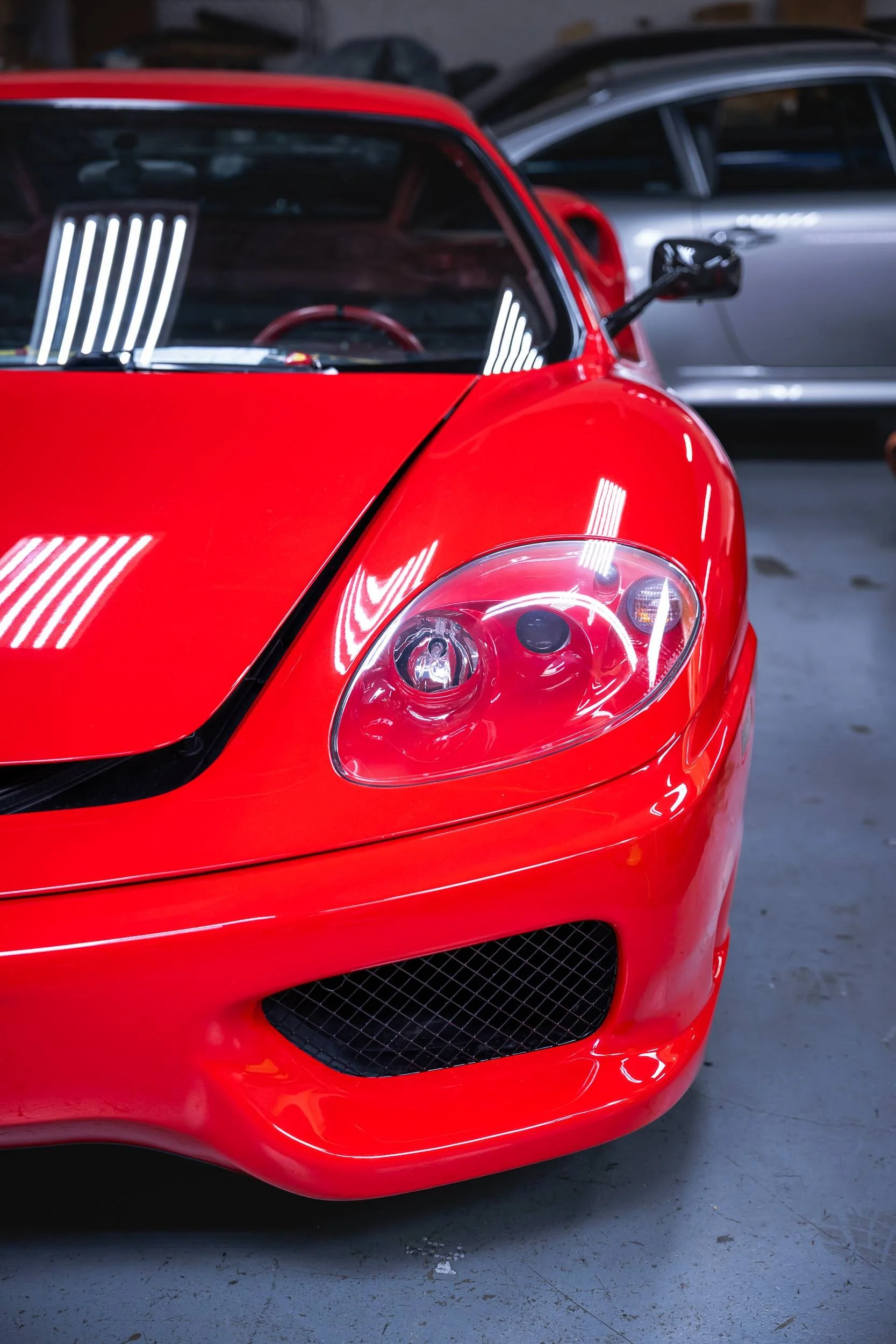 Close-up of a red sports car's front end, showing the headlight, front grille, and part of the hood.