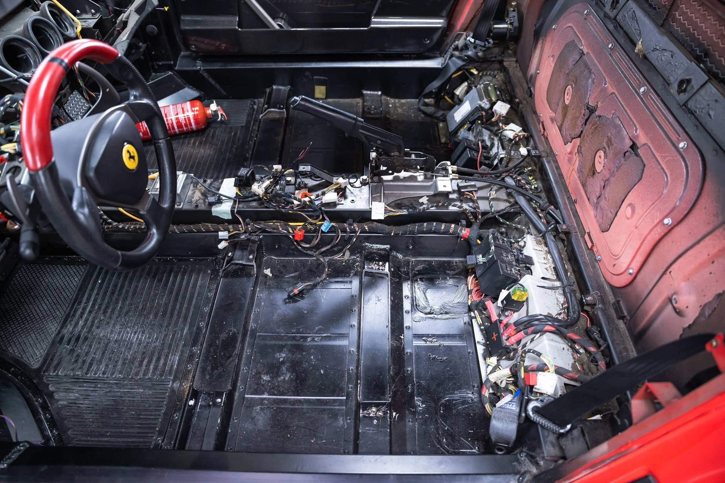 Interior of a race car with the dashboard and seats removed, exposing wiring, electronics, and metal framework.