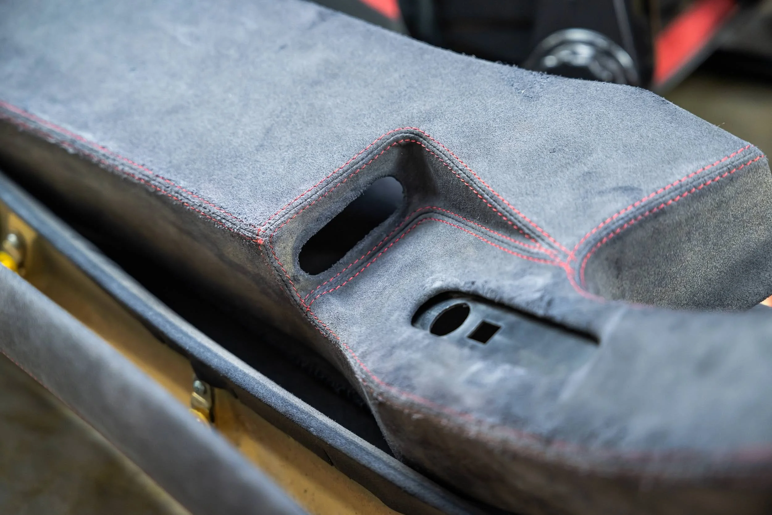 Close-up of a gray suede car interior panel with red stitching and a vent opening.