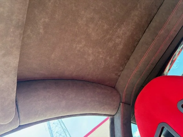 Close-up of car interior showing brown fabric roof, red seat, and part of the window with a view of the sky and a power line outside.