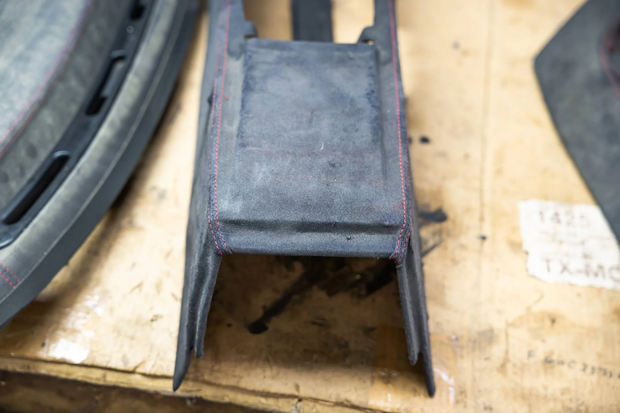 A black, rectangular rubber step with red stitching on the sides, attached to a metal frame on a wooden surface.