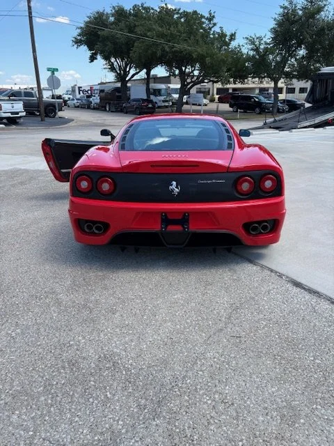 Red Ferrari sports car parked in an outdoor lot with the trunk open.