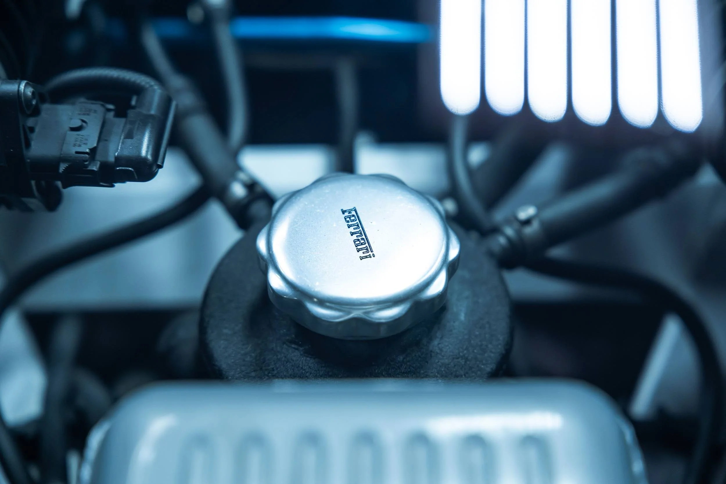 Close-up of a motorcycle engine with a metallic oil cap labeled 'YUBER' and chrome components, with a blurred background of engine parts.