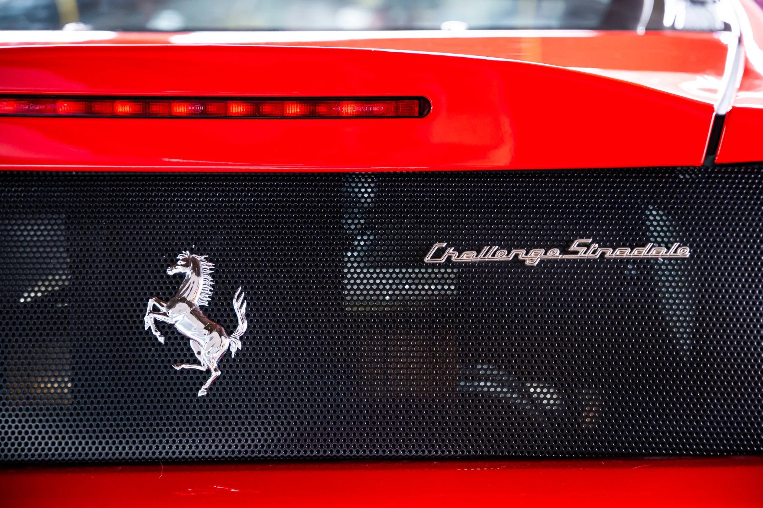 Close-up of a red sports car's rear end, featuring a black grille with a prancing horse emblem, and the text "Challenger SRT" on the grille.