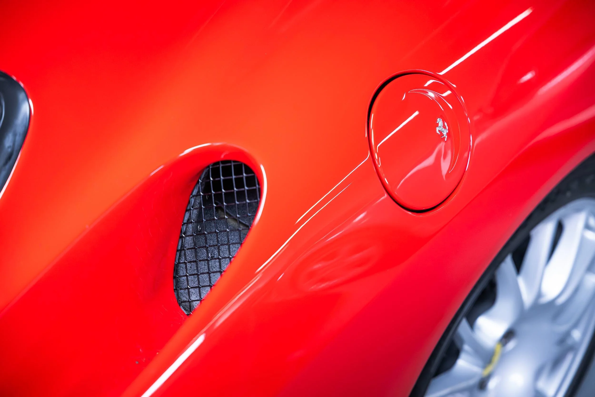 Close-up of a red sports car's front fender with a Ferrari logo on the wheel cover and an air intake vent with a black grille.