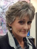 Close-up of a smiling woman with short, gray hair wearing a dark jacket and a plaid shirt.
