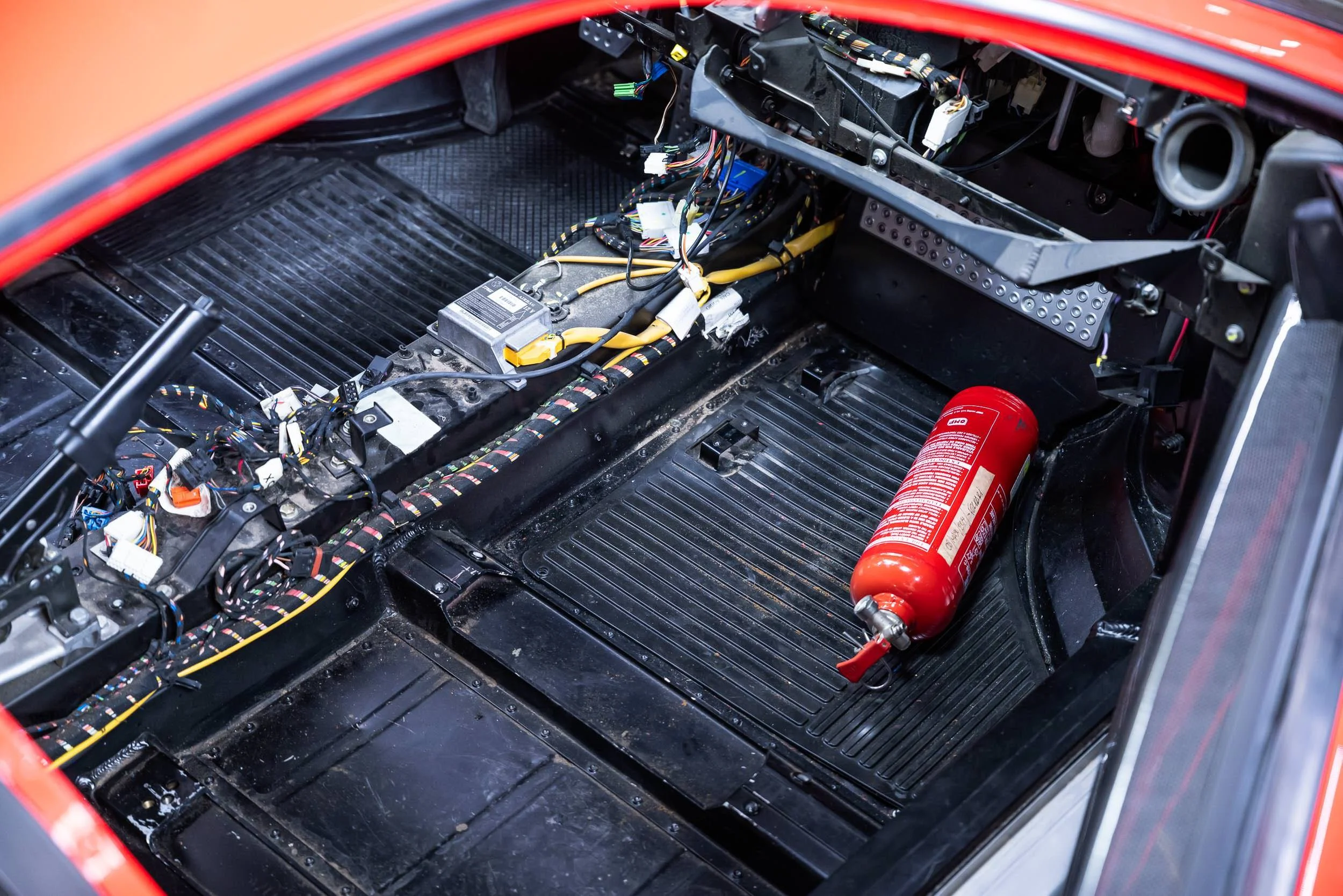 The interior of a race car showing exposed wiring and electronic components, with a fire extinguisher mounted inside.