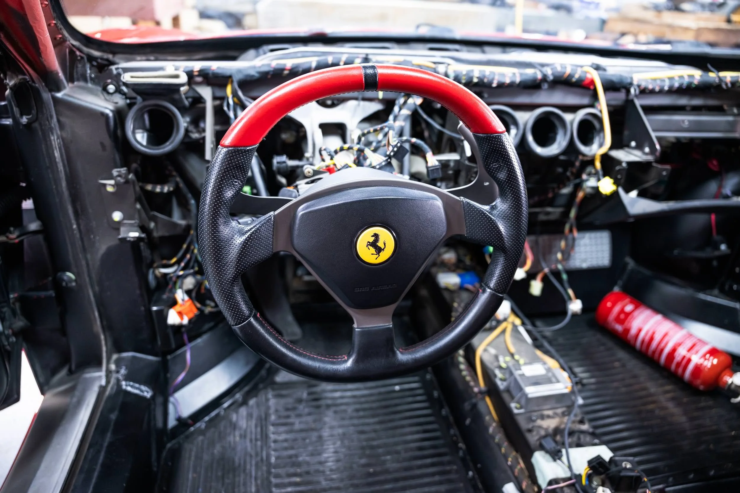 Interior of a car dashboard being assembled with exposed wires and a steering wheel with a Ferrari logo.
