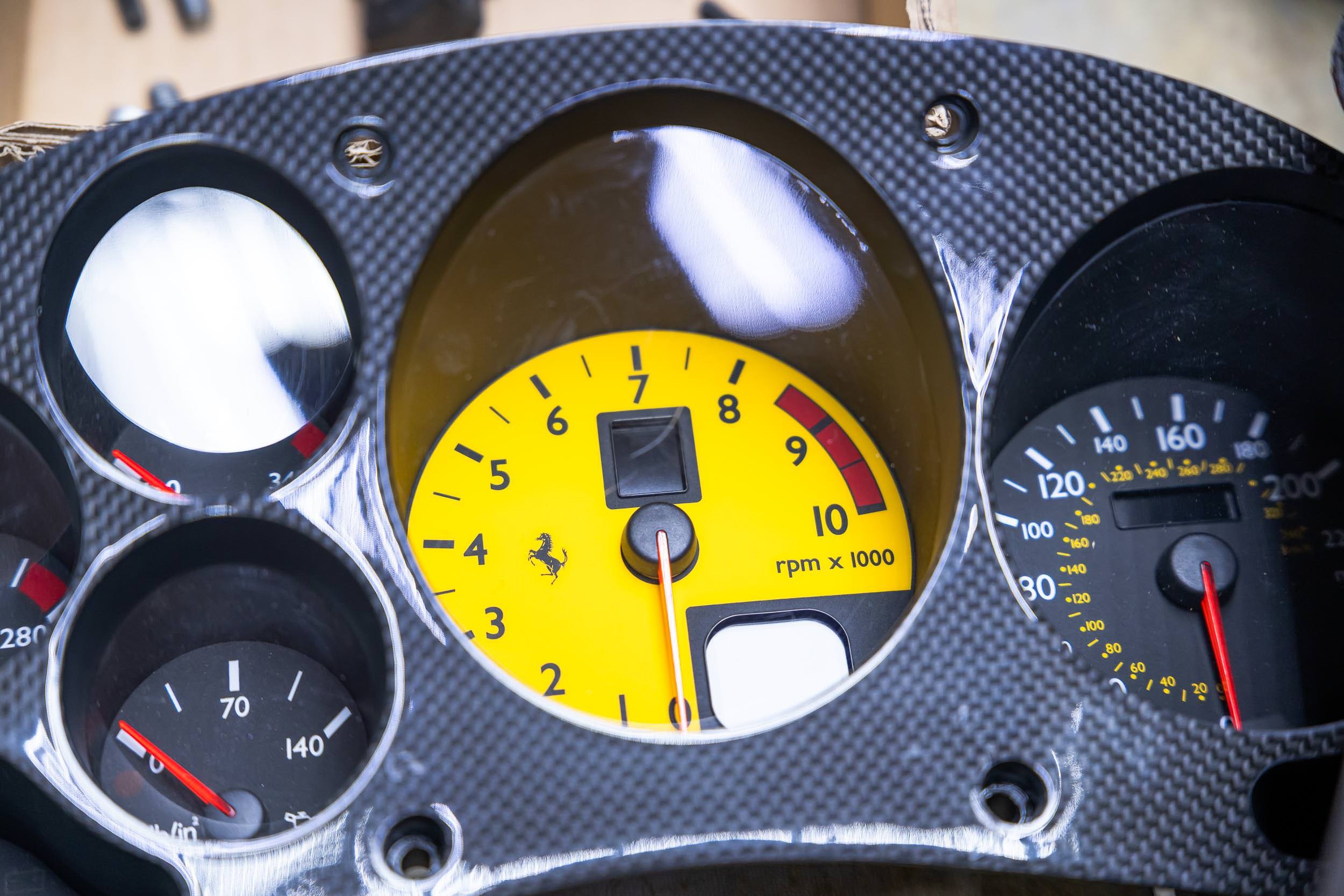 Close-up of a car dashboard gauge cluster featuring multiple dials, including a yellow tachometer with a prancing horse logo, indicating the engine's revolutions per minute, with other gauges showing speed, temperature, and oil pressure.