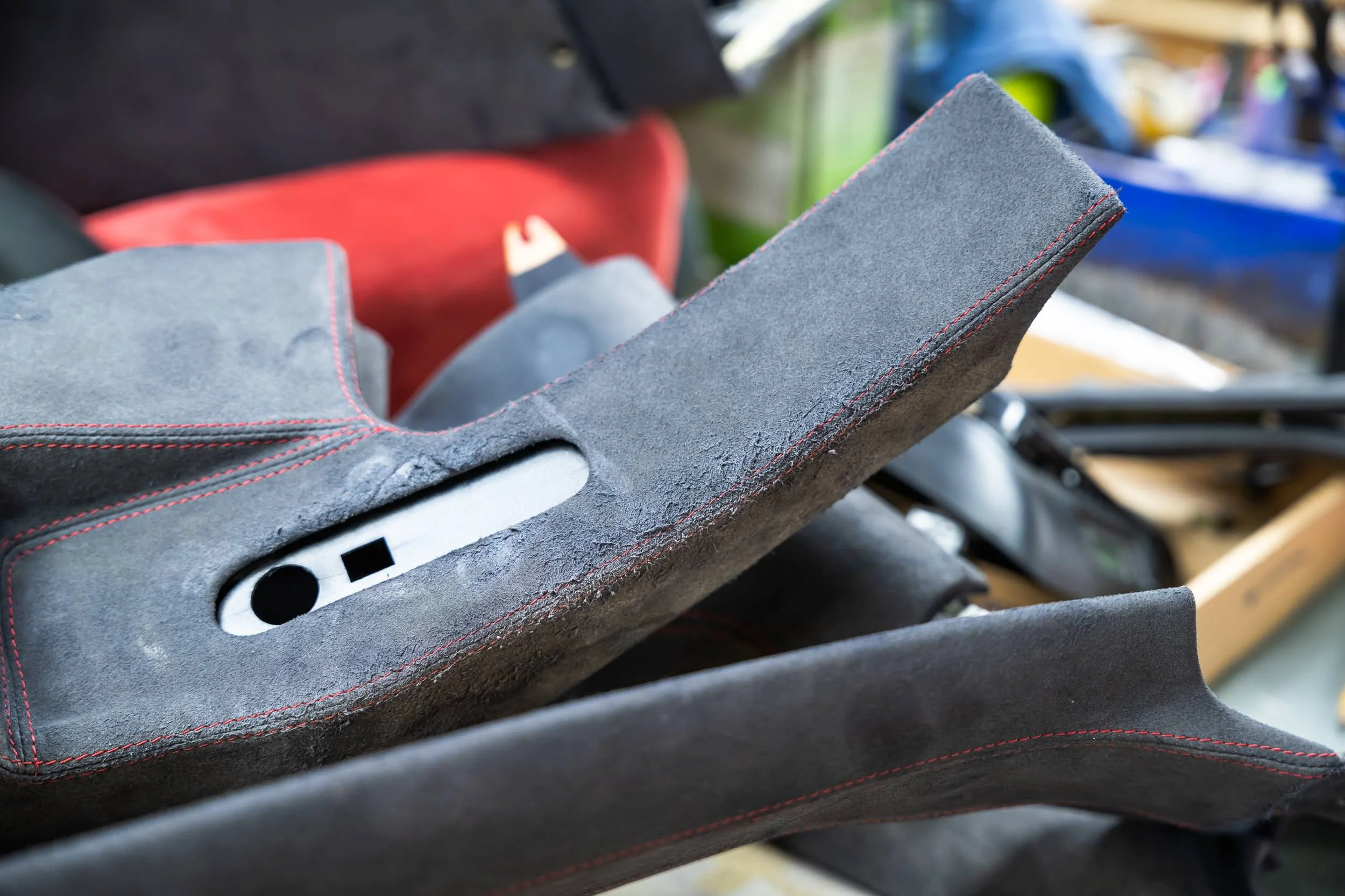 Close-up of a rough, textured gray leather surface with red stitching, next to a black surface with red accents, in a workshop or store setting.