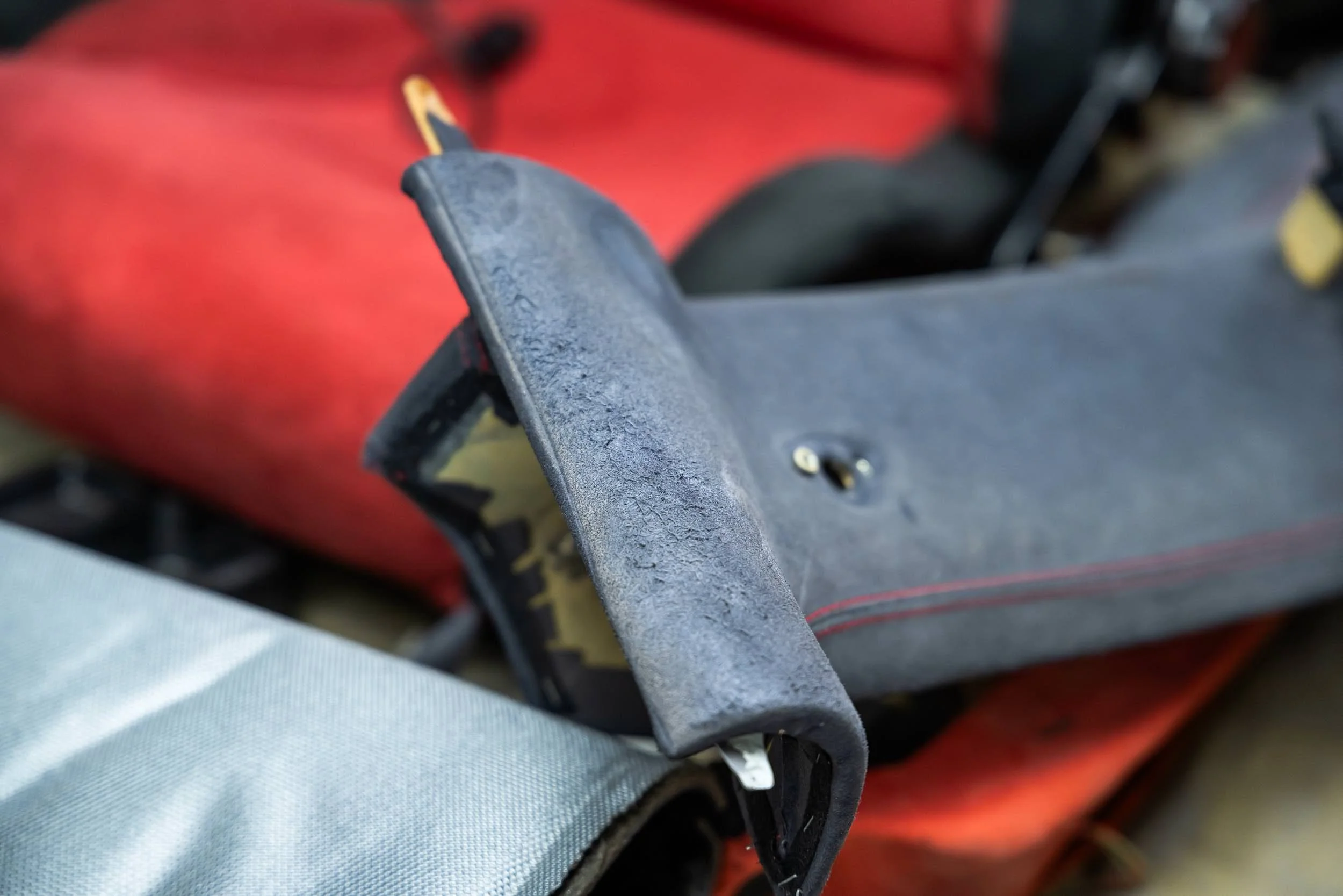 Close-up of a black plastic handle or lever with some scratches and a small screw, against a blurred red background, with part of a person's attire visible at the bottom.