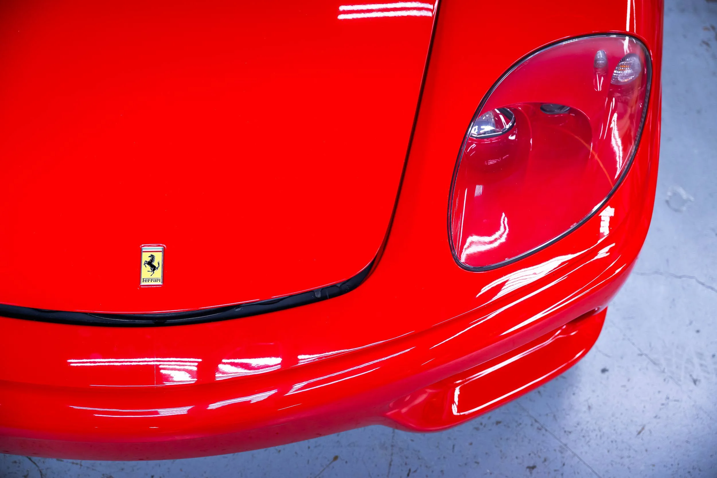 Close-up of the front of a red Ferrari sports car, showing the Ferrari emblem, headlight, and part of the curved body.