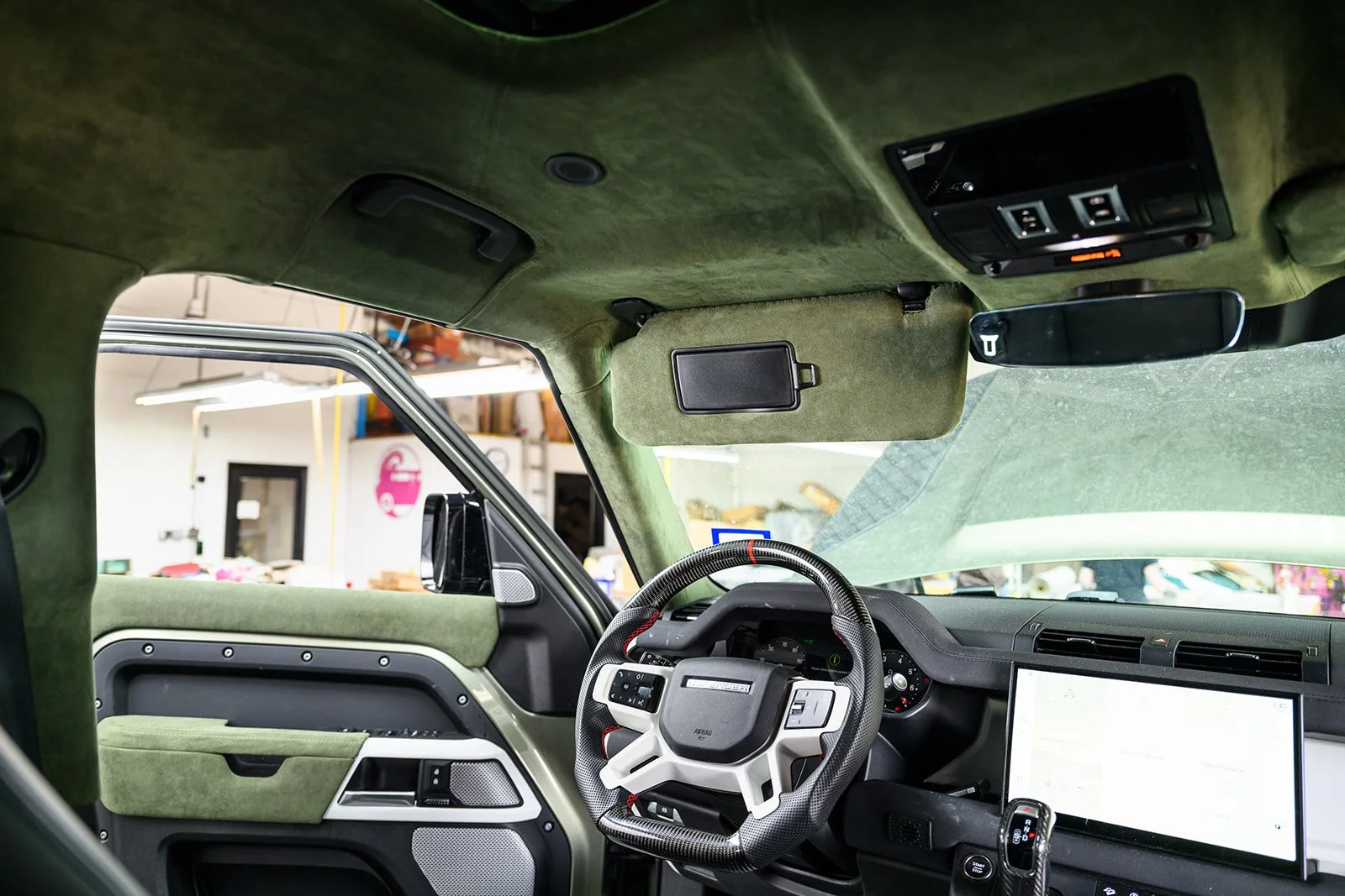 The interior of a vehicle with a green suede or fabric roof lining, dashboard, and steering wheel in a warehouse or garage setting.