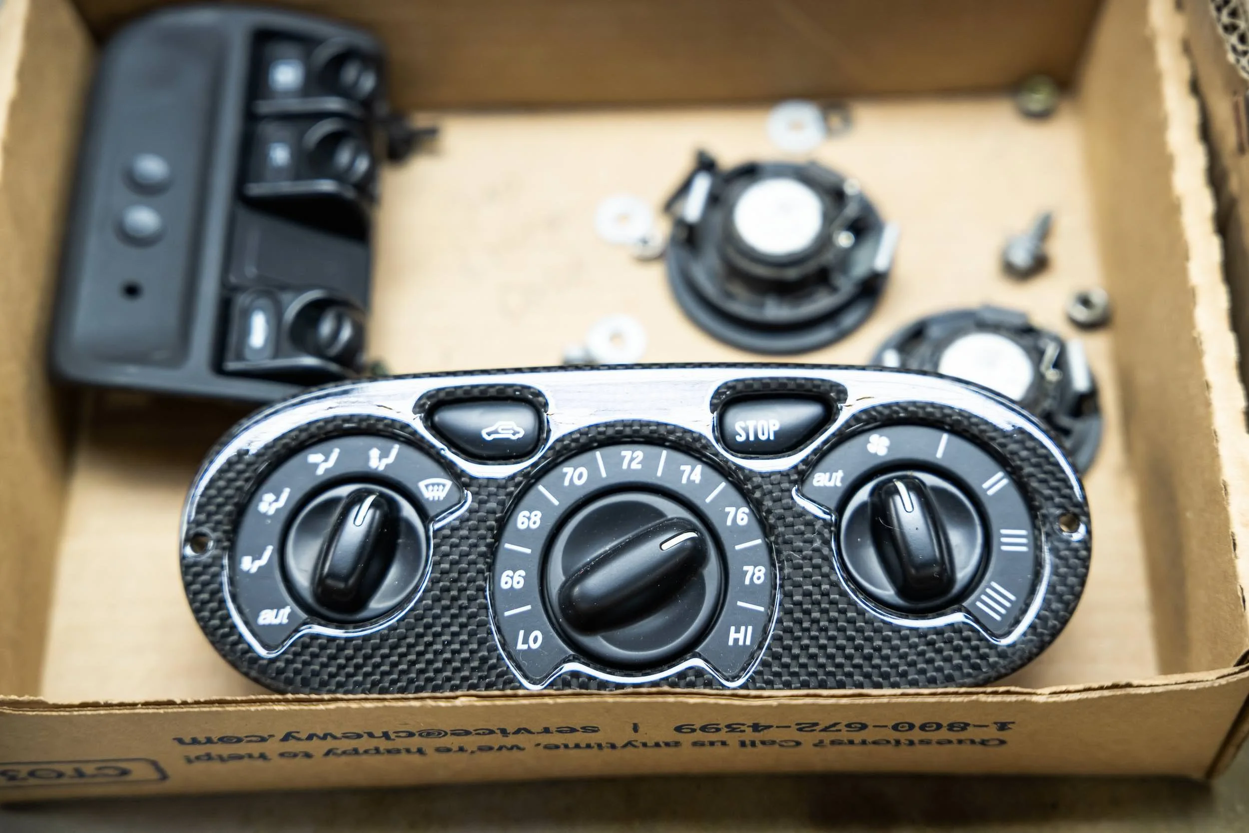 A car climate control panel with dials for temperature, fan speed, and air distribution, placed inside a cardboard box.