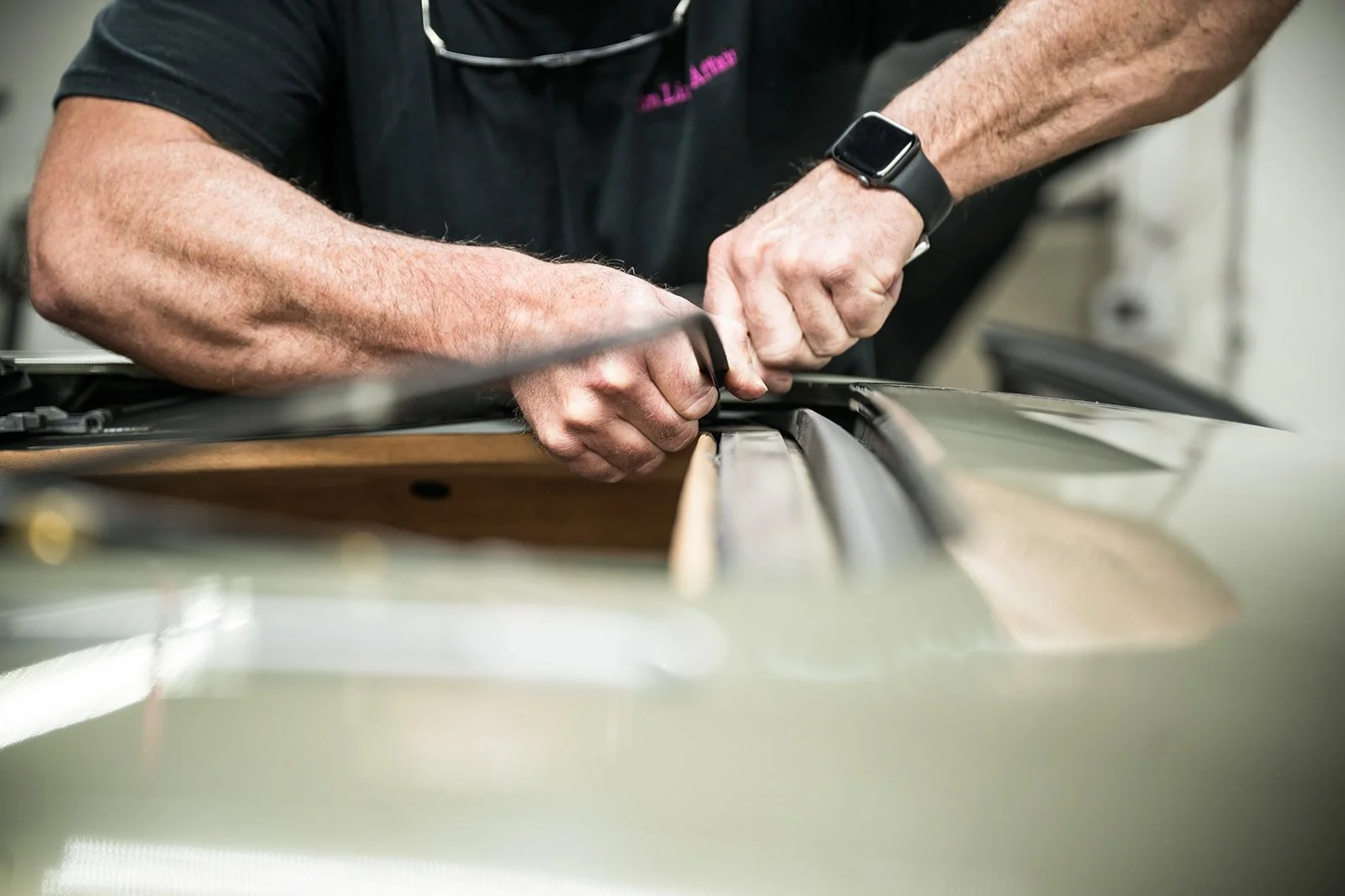 Person working on a car's hood, using a tool, with a smartwatch on their wrist.