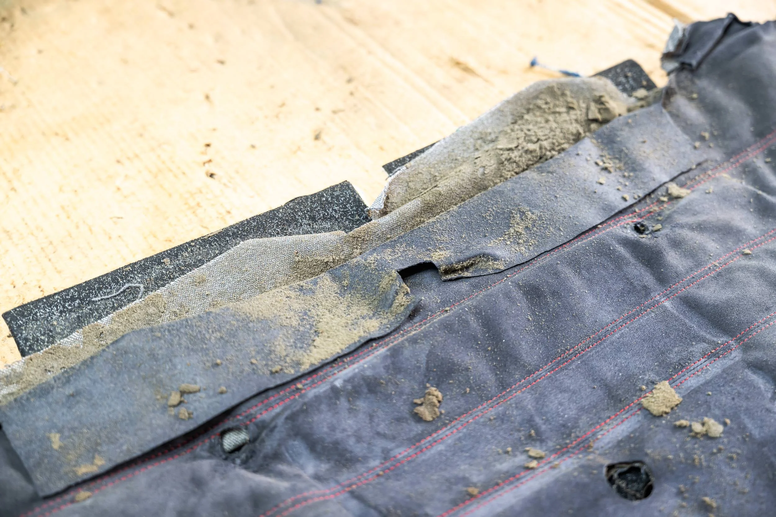 Close-up of a roof flashing installation process with black roofing material, adhesive strips, and dirt or debris on a wooden surface.