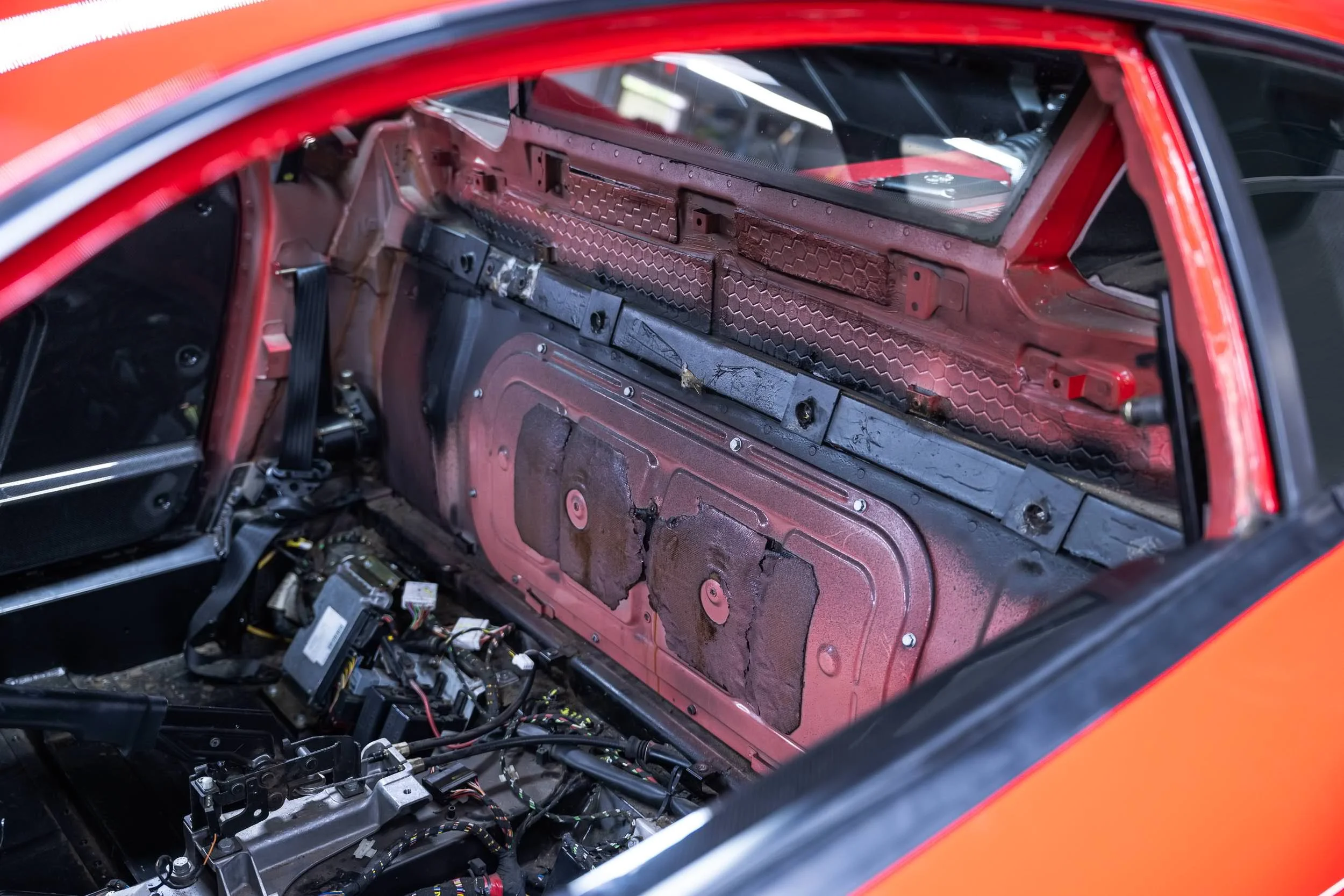 The interior of a disassembled car shows wiring and metal components with the dashboard removed, revealing internal structures.