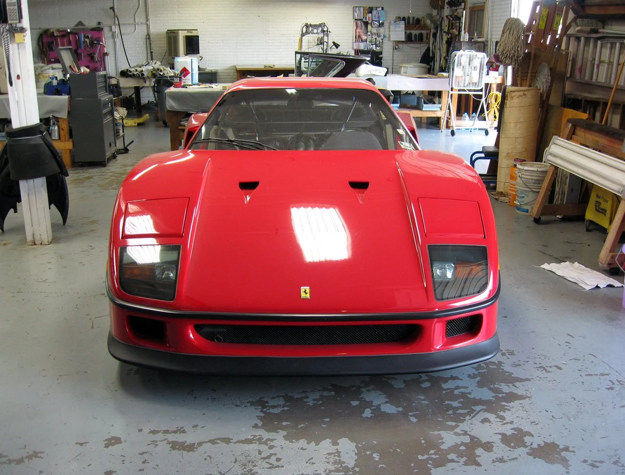 Red Ferrari sports car parked inside a workshop with tools and equipment in the background.
