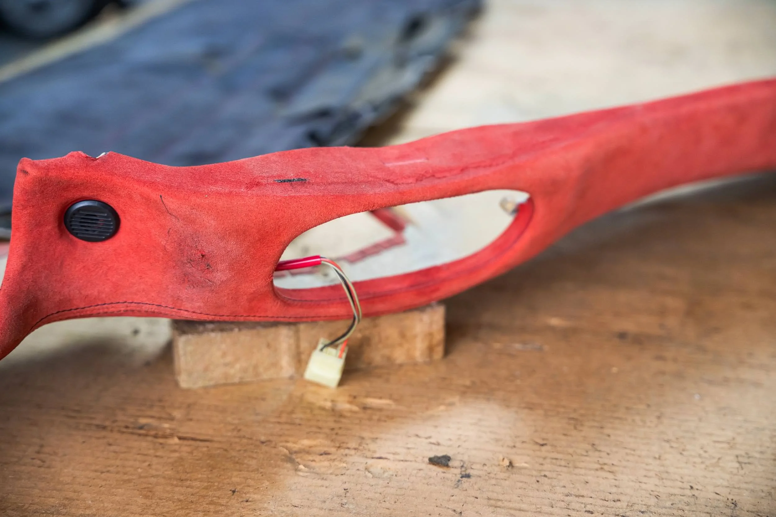 Close-up of a red plastic or rubber object with a black speaker-like component and some wiring, placed on a wooden surface.
