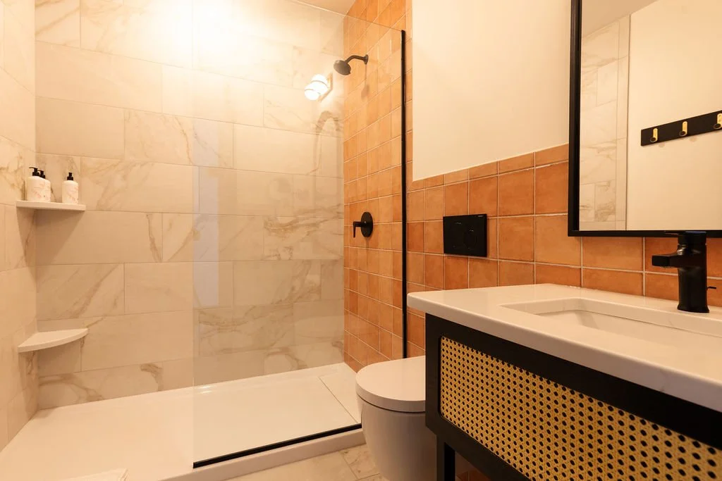 Modern bathroom with a walk-in shower, white marble tiles, terracotta tiles on one wall, a white toilet, and a black and white vanity with a mirror.