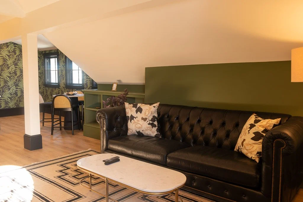 Living area of the Downtown Luxury Condo at Hotel Thaxter in Portsmouth, New Hampshire, featuring a tufted black leather couch.