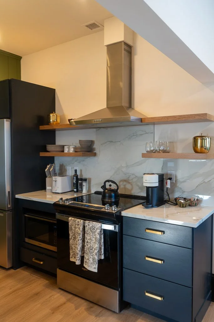 Kitchen with stove, hood, open shelves, black cabinets, and refrigerator in the Downtown Luxury Condo at Hotel Thaxter in Portsmouth, New Hampshire.