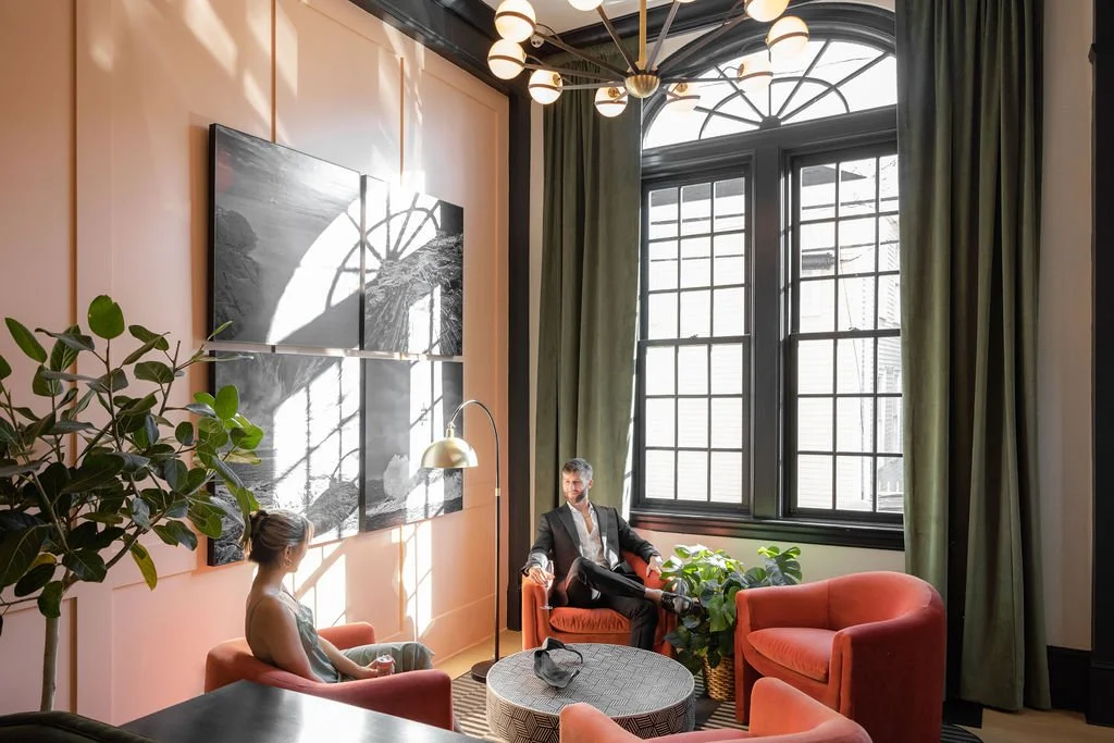 Guests relaxing in Hotel Thaxter’s sunlit lobby with tall historic windows, velvet seating, and modern boutique design in downtown Portsmouth, New Hampshire.