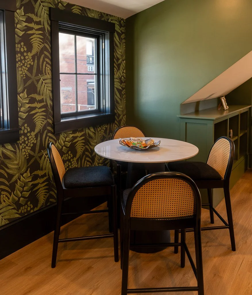 Small round counter-height table with four chairs in a corner with green botanical wallpaper and green accent wall in the Downtown Luxury Condo at Hotel Thaxter in Portsmouth, New Hampshire.