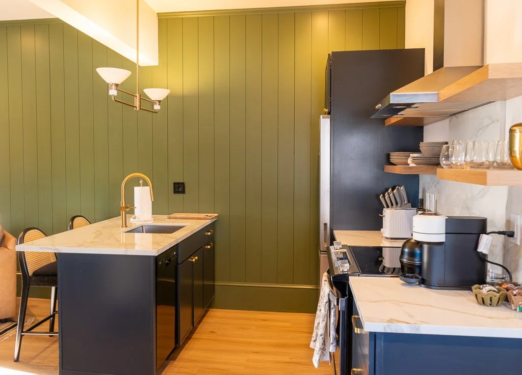 Kitchen island with counter seating, green accent wall, and gold pendant light in the Downtown Luxury Condo at Hotel Thaxter in Portsmouth, New Hampshire.
