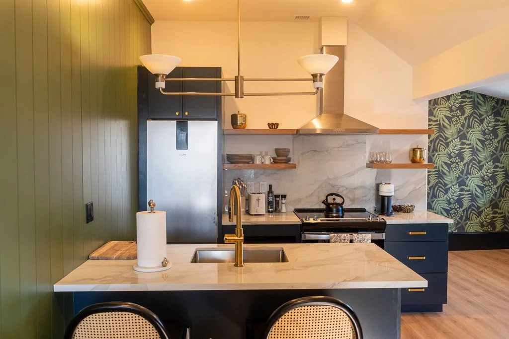 Full kitchen with counter seating, open shelves, and a green accent wall at Hotel Thaxter in Portsmouth, New Hampshire.