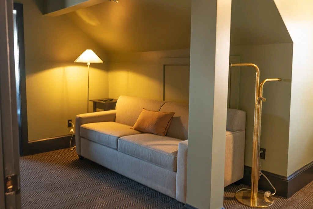 Fold-out couch in TV room with lamp on in the Downtown Luxury Condo at Hotel Thaxter in Portsmouth, New Hampshire.