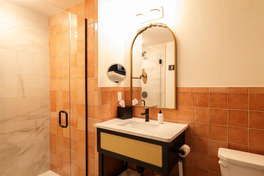 Bathroom with a glass shower door, a wall-mounted mirror, and a black vanity with a white sink and soap dispenser.