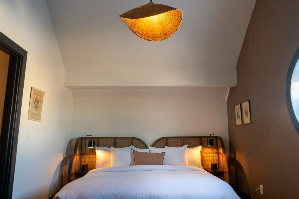 Bedroom of the Downtown Luxury Condo at Hotel Thaxter in Portsmouth, New Hampshire, featuring a rattan bed frame and warm bedside lamps.