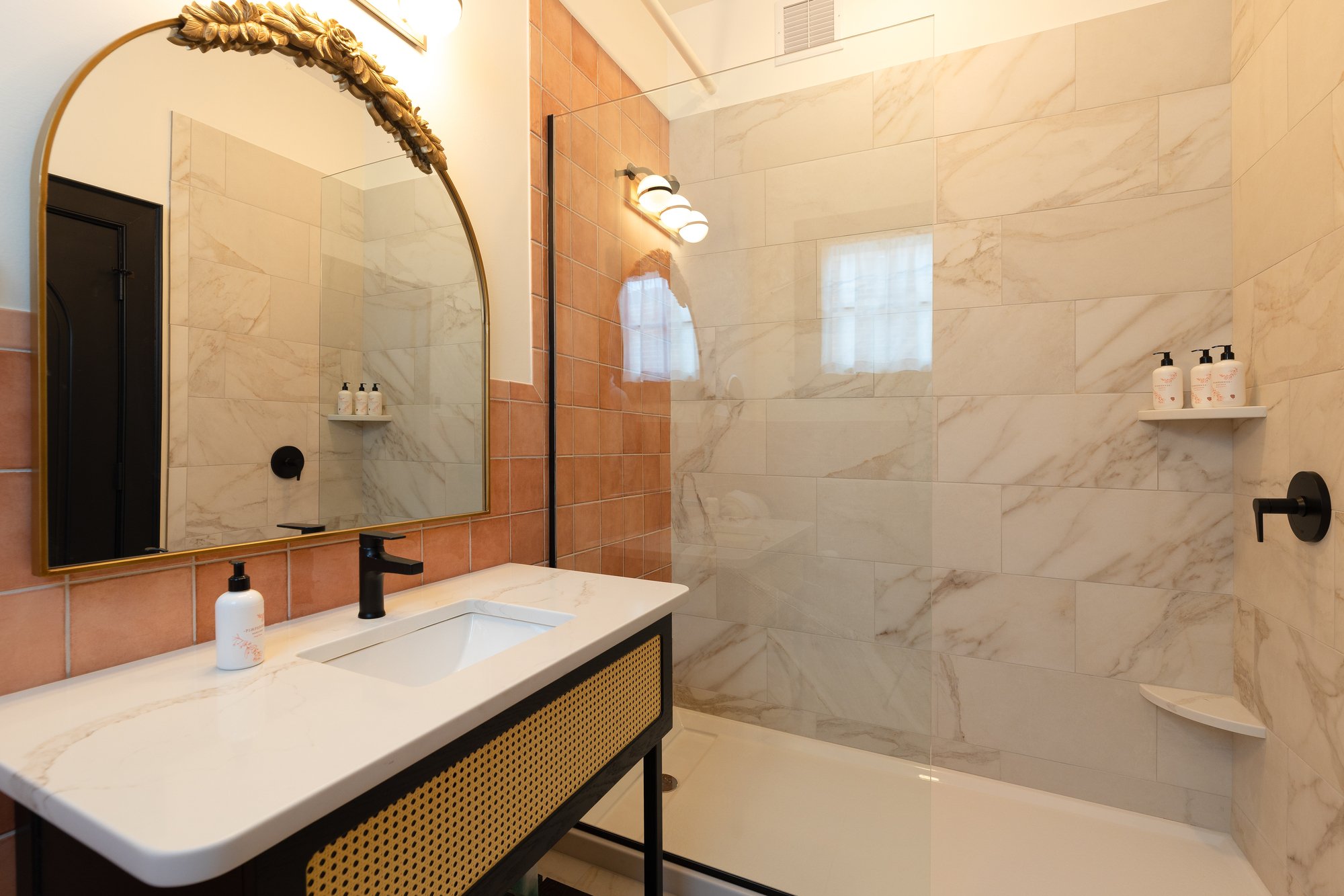 Modern bathroom with a large marble-tiled shower, a white sink with a black faucet, and a mirror with a decorative gold frame.